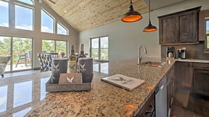 A spacious kitchen with granite countertops, dark wooden cabinets, and pendant lighting. - Lavish Retreat w/ Decks, Steps to Table Rock Lake! (Lampe)