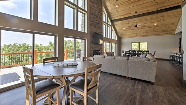 A spacious room with a large dining table, wooden chairs, a sofa, and a ceiling fan. - Lavish Retreat w/ Decks, Steps to Table Rock Lake! (Lampe)