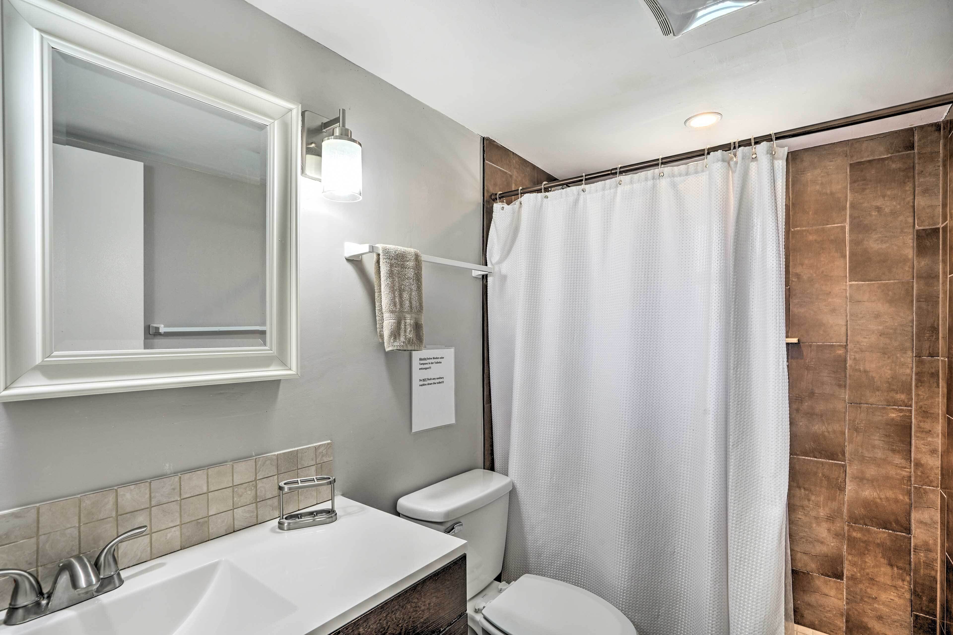 Un baño con un lavabo blanco, un inodoro, cortina de ducha y una toalla colgada en un perchero.