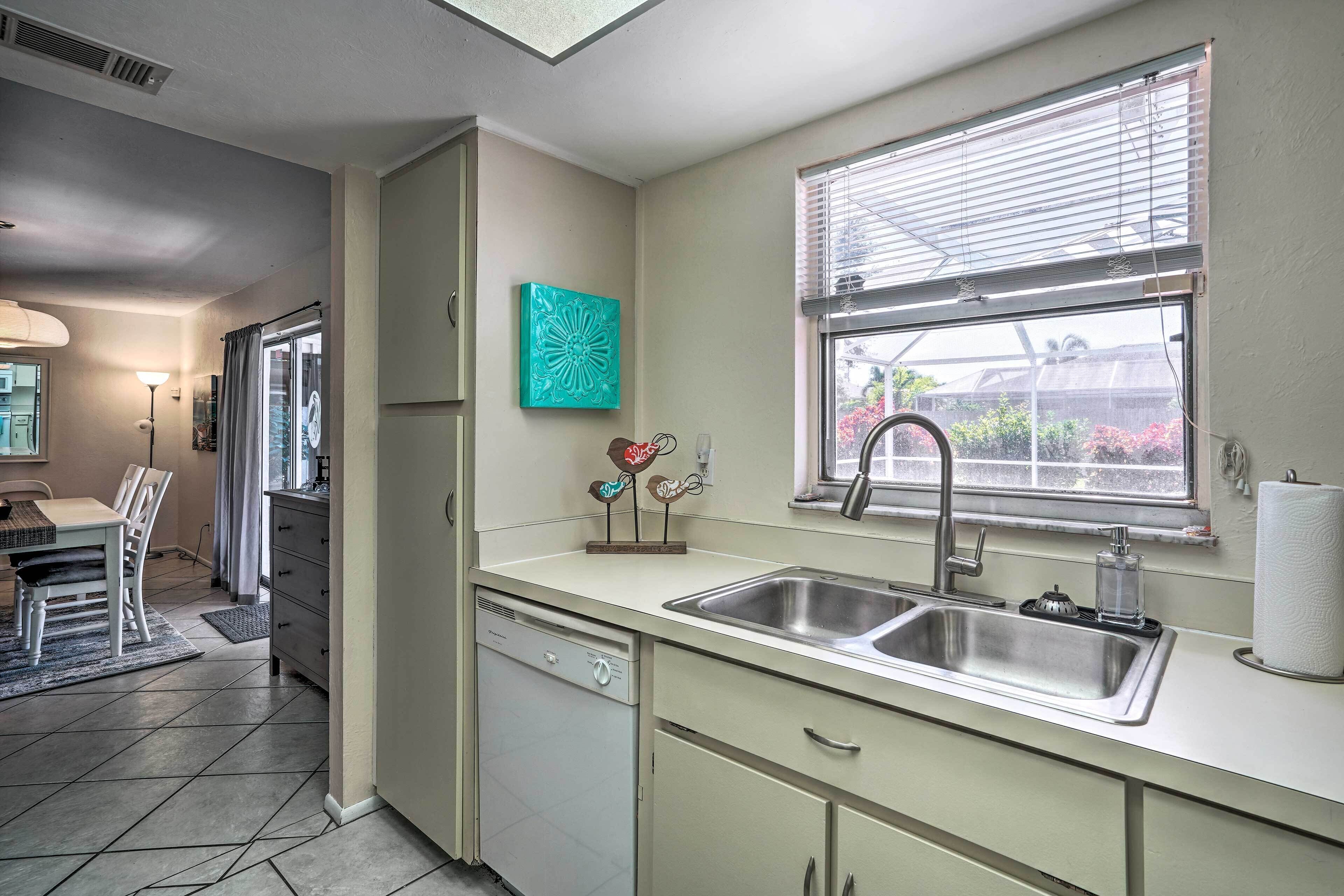 A compact kitchen with a dishwasher, double sink, and a window with blinds.