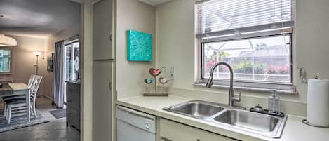 A compact kitchen with a dishwasher, double sink, and a window with blinds.