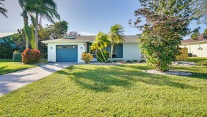 A single-story house with a blue garage, surrounded by well-maintained lawns and palm trees. - 7 Mi to Beaches: Pet-friendly Cape Coral Home (Cape Coral)