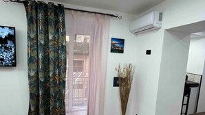 A room with a wooden floor, a window with a curtain, an air conditioning unit, and a framed picture on the wall. - CaBi's Dreams (Napoli)