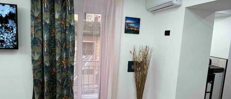 A room with a wooden floor, a window with a curtain, an air conditioning unit, and a framed picture on the wall.