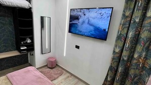 A modern bedroom with a bed, a TV mounted on the wall, a mirror, and a small pink stool. - CaBi's Dreams (Napoli)