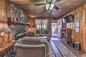 A cozy cabin interior with a stone fireplace, a sofa, a television, and a wooden ceiling. - Rustic Ruidoso Vacation Rental ~ 2 Mi to Downtown! (Ruidoso)