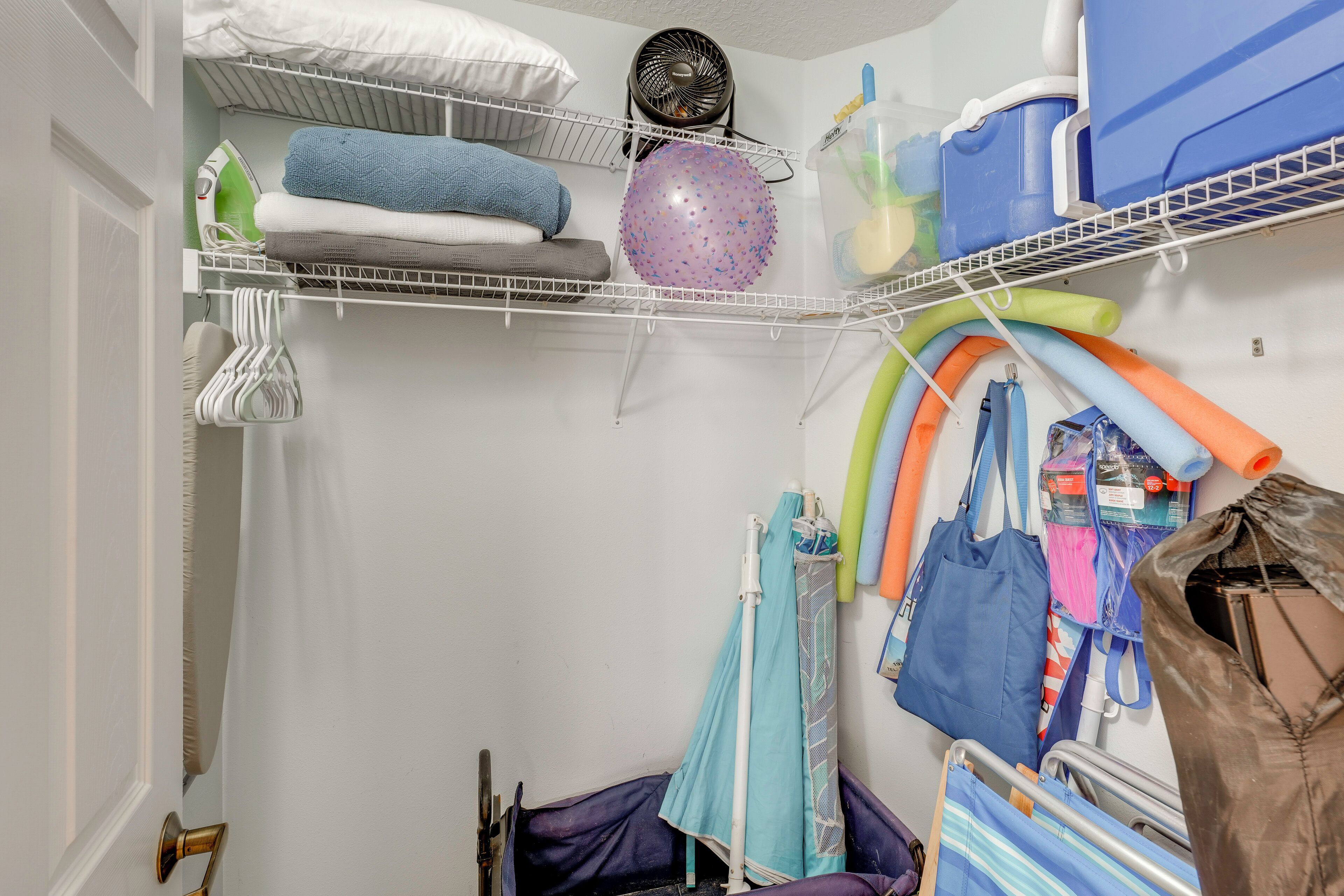 A storage closet with shelves holding folded towels, a fan, and various containers.