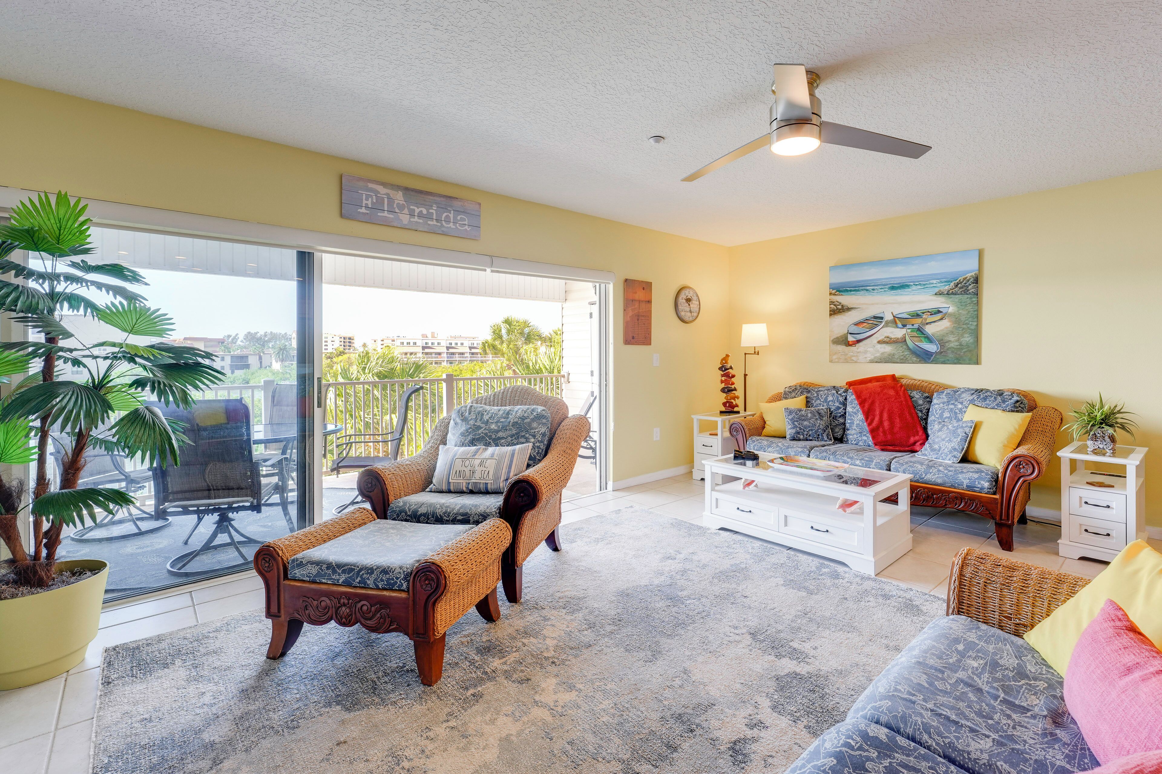 A living room with a sofa, armchairs, a coffee table, a potted plant, and a painting of boats on a beach.