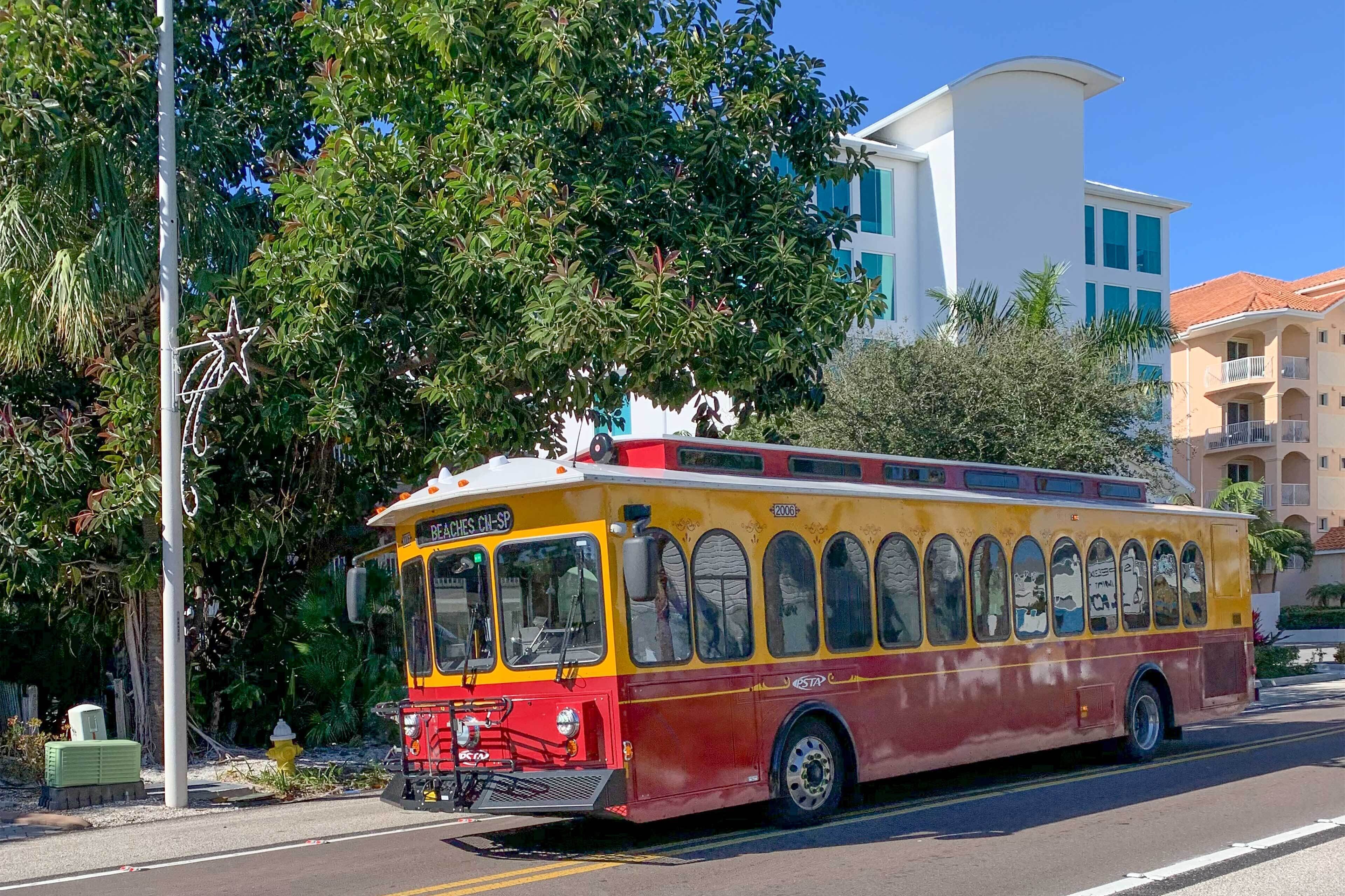 A colorful bus with a red and yellow exterior, parked on a street with buildings and trees in the background.