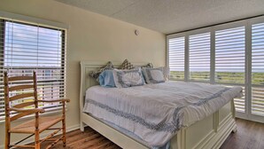 A bedroom with a large bed, wooden floor, and a chair. - Welcoming Brigantine Condo w/ Ocean Views! (Brigantine)