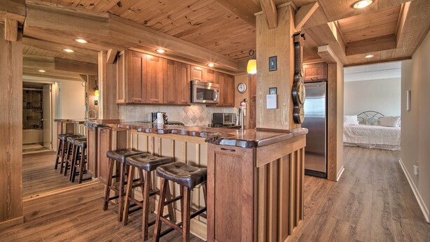 A kitchen with wooden cabinets, a stainless steel refrigerator, a microwave, and a bar area with stools. - Welcoming Brigantine Condo w/ Ocean Views! (Brigantine)