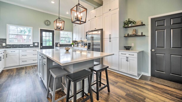 A modern kitchen with white cabinetry, a large island with stools, a stainless steel refrigerator, and pendant lighting. - Spacious Abode, Walk to Texas Heroes Square! (Gonzales)