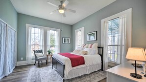 A bedroom with a bed, a chair, a desk, a ceiling fan, and large windows. - Spacious Abode, Walk to Texas Heroes Square! (Gonzales)