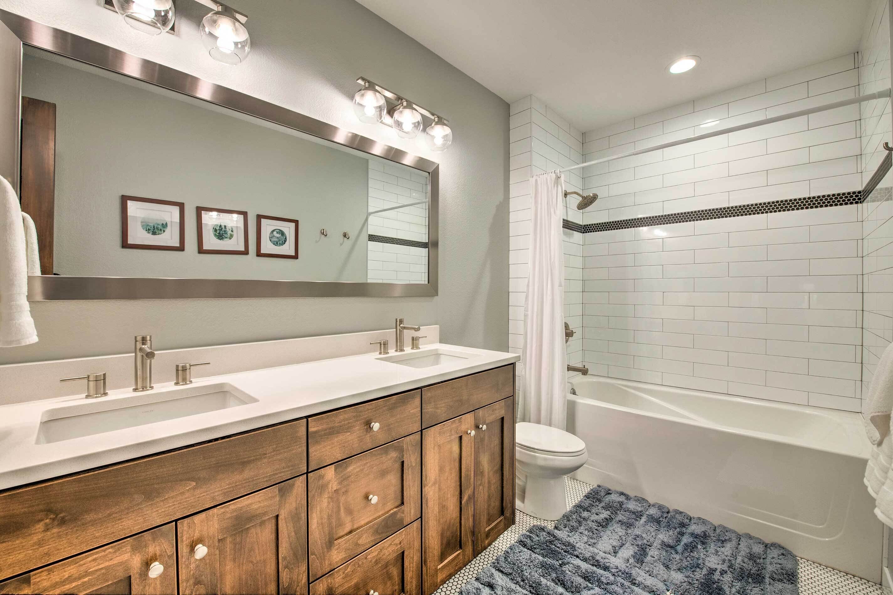 A bathroom with a double sink vanity, a large mirror, a toilet, and a bathtub.