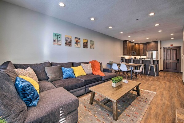 A modern living room with a sectional sofa, a wooden coffee table, and a kitchen area with bar stools.