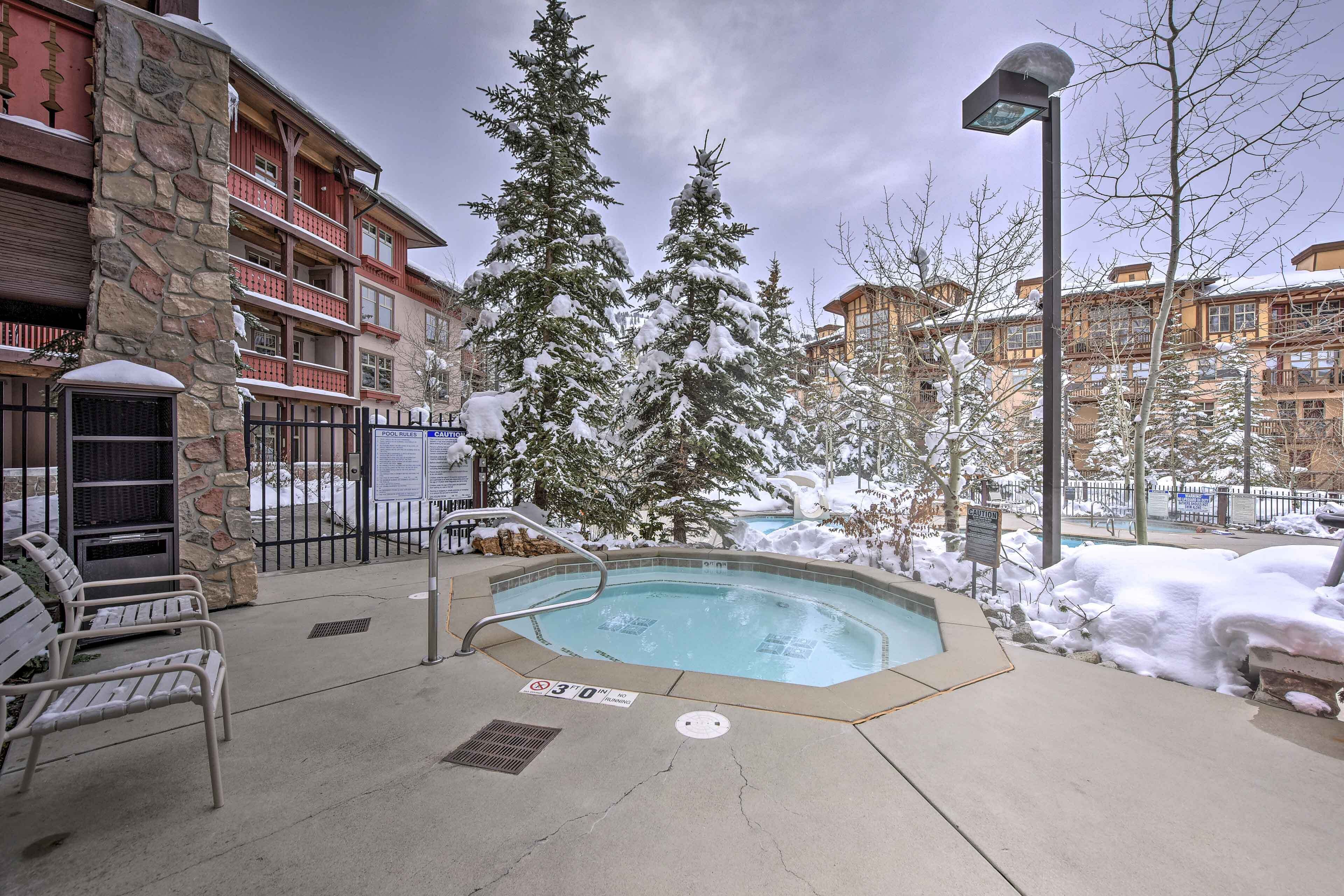 A pool area with a hot tub, benches, and a stone wall.