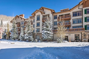 A multi-story hotel with balconies and large windows, surrounded by snow-covered trees and a clear sky.