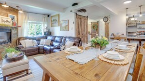 A modern living room with a wooden dining table set for six, a leather sofa, and a kitchen area visible in the background. - Farmhouse w/ Private Hot Tub < 1 Mile to Birch Bay (Blaine)