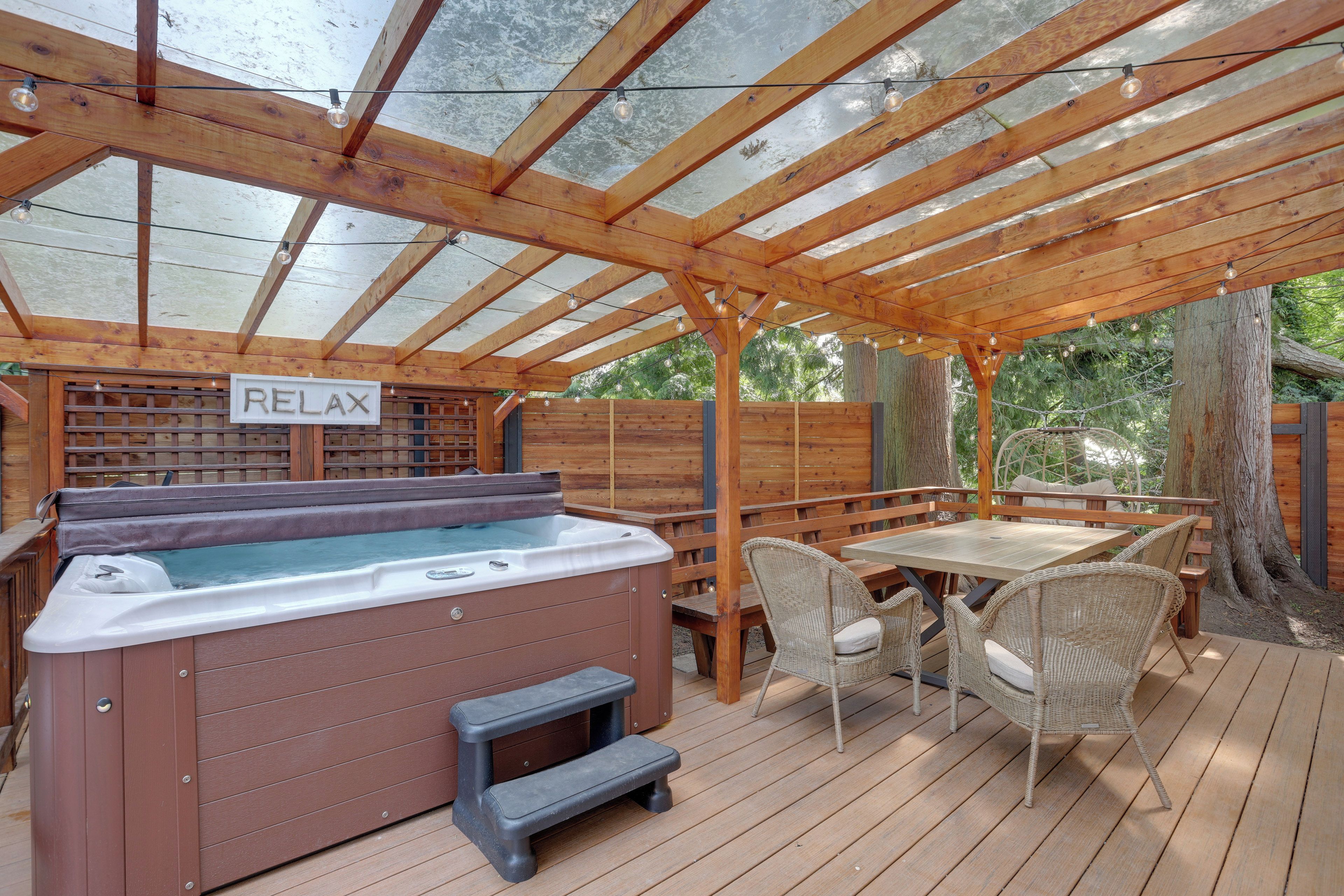 Een houten terras met een jacuzzi, rieten stoelen en een tafel.