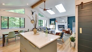 A modern kitchen with a central island, dining area with chairs, and a living room with a sofa and fireplace.