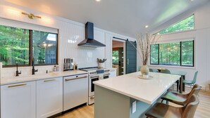 A modern kitchen with white cabinetry, stainless steel appliances, and large windows offering views of greenery.
