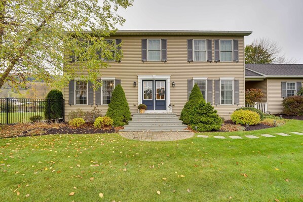 A two-story house with a front porch, a small garden, and a black metal fence. - Lakefront Homer Abode w/ Patio & Backyard! (Homer)