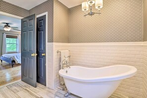 A bathroom with a freestanding bathtub, a door with a towel hanging on it, and a patterned wall. - Lakefront Homer Abode w/ Patio & Backyard! (Homer)