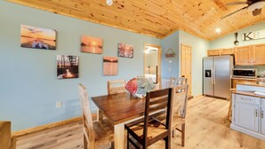 A wooden ceiling, a dining table with chairs, a kitchen area with cabinets and appliances, and wall-mounted artwork. - Cozy Waverly Cabin w/ Fireplace & Deck! (Waverly)