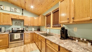 A kitchen with wooden cabinets, granite countertops, a built-in oven, and a coffee maker. - Cozy Waverly Cabin w/ Fireplace & Deck! (Waverly)