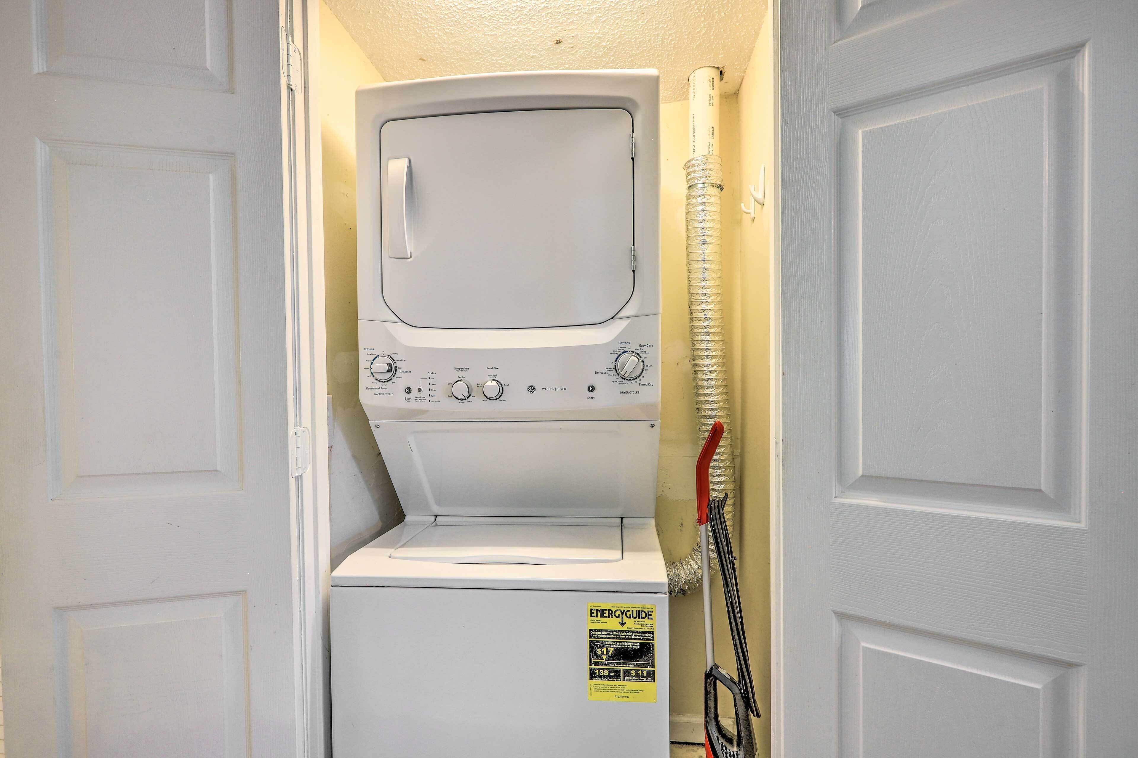 A compact laundry room with a front-loading washer and dryer, a visible energy efficiency label, and a hose for water connection.