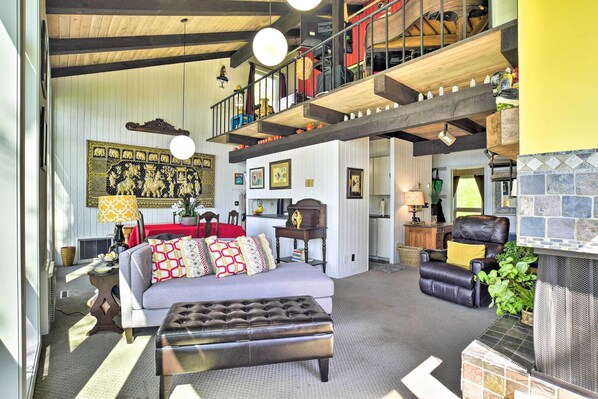 A spacious living room with a grey sofa, a black leather chair, and a fireplace. There is a wooden staircase with a red railing leading to an upper level. - Hilltop Green Lake Home: Dock, Kayaks, Views! (Princeton)