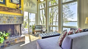 A cozy living room with a stone fireplace, large windows overlooking a lake, and comfortable seating. - Hilltop Green Lake Home: Dock, Kayaks, Views! (Princeton)
