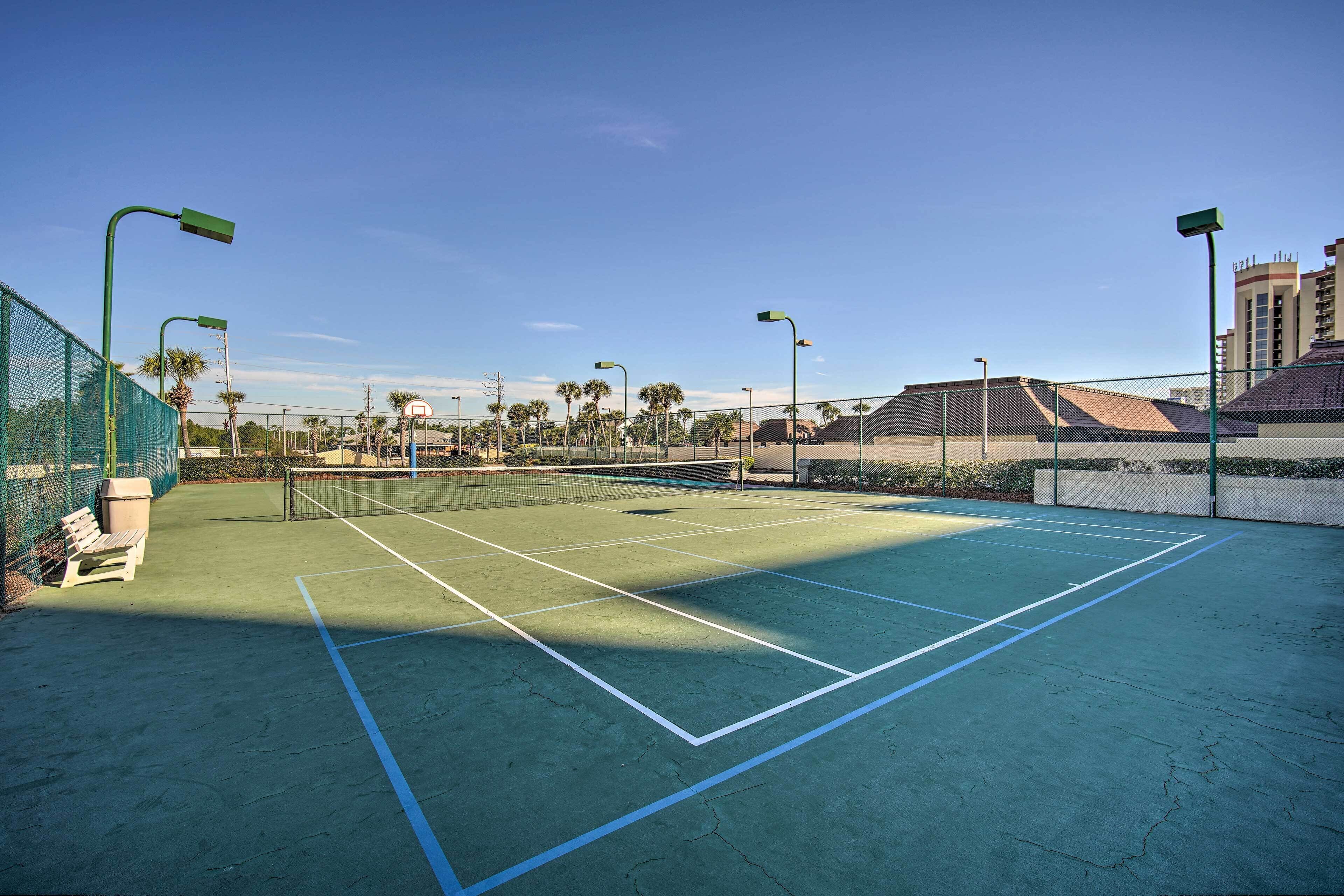 Una cancha de tenis al aire libre con superficie verde, líneas divisorias blancas y vallas perimetrales.