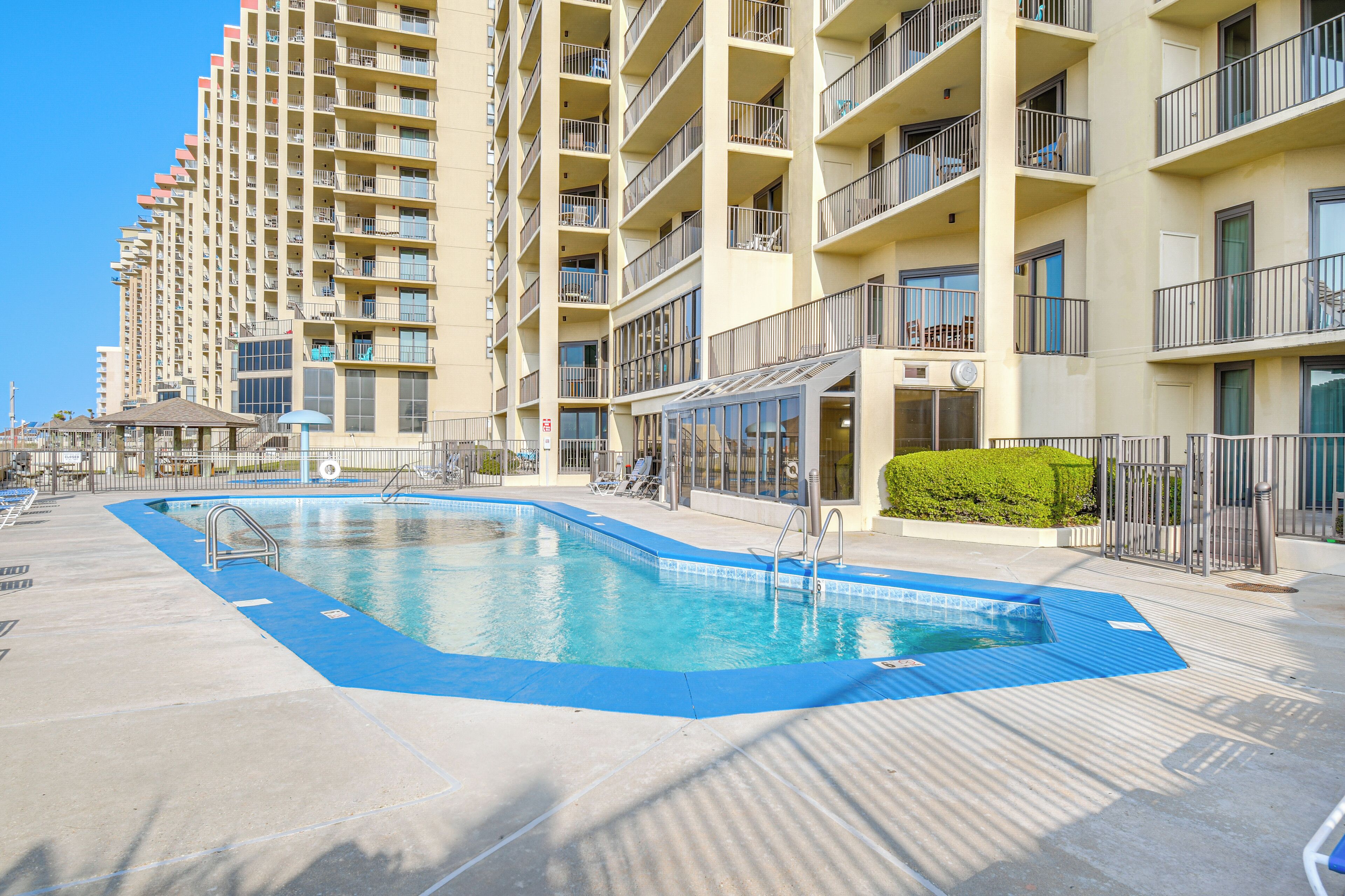 A swimming pool with a blue deck, surrounded by a high-rise building with balconies.