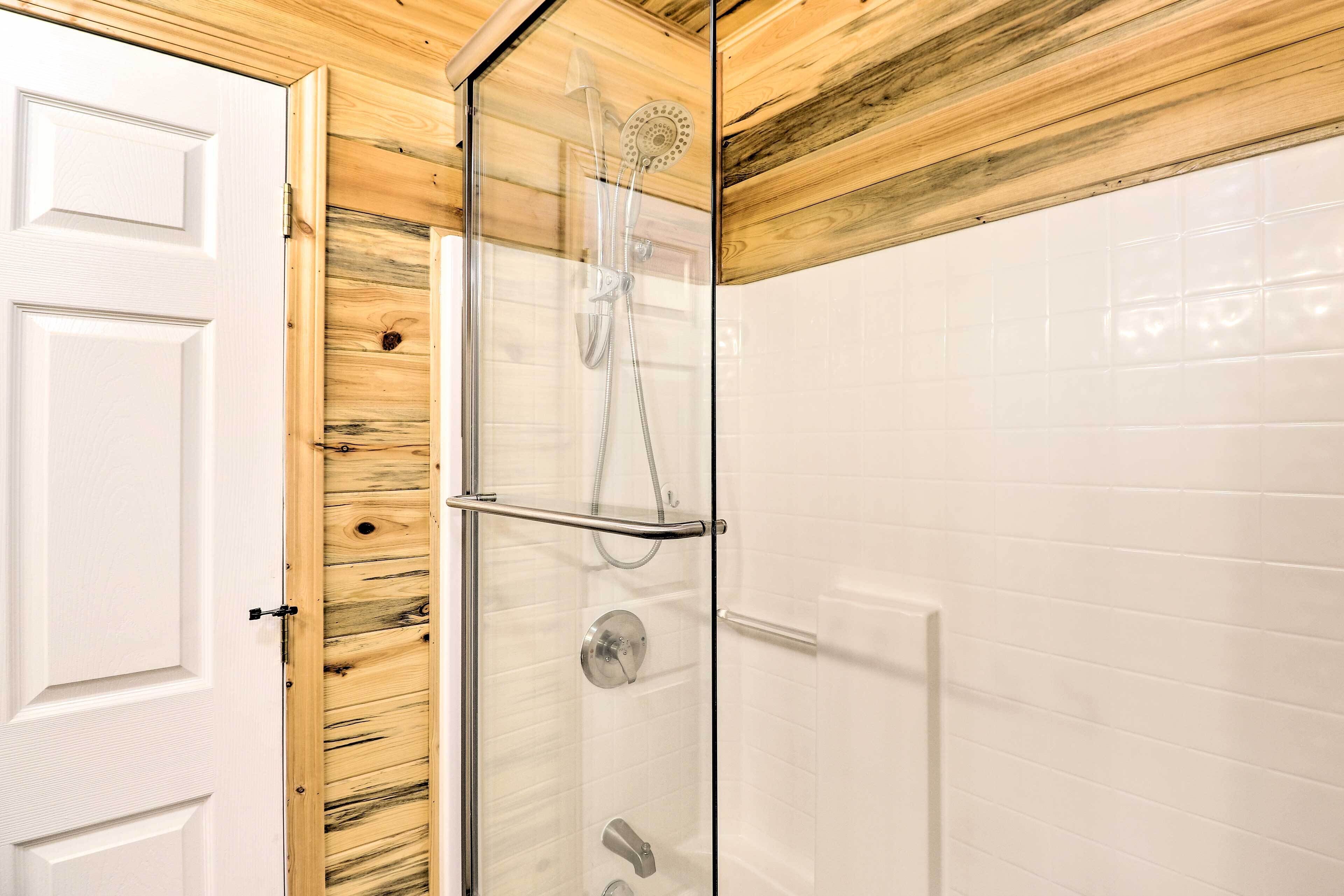 Un baño con ducha de vidrio, paredes de azulejos blancos y techo de madera.