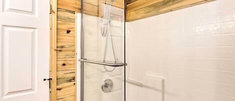 Un baño con ducha de vidrio, paredes de azulejos blancos y techo de madera.