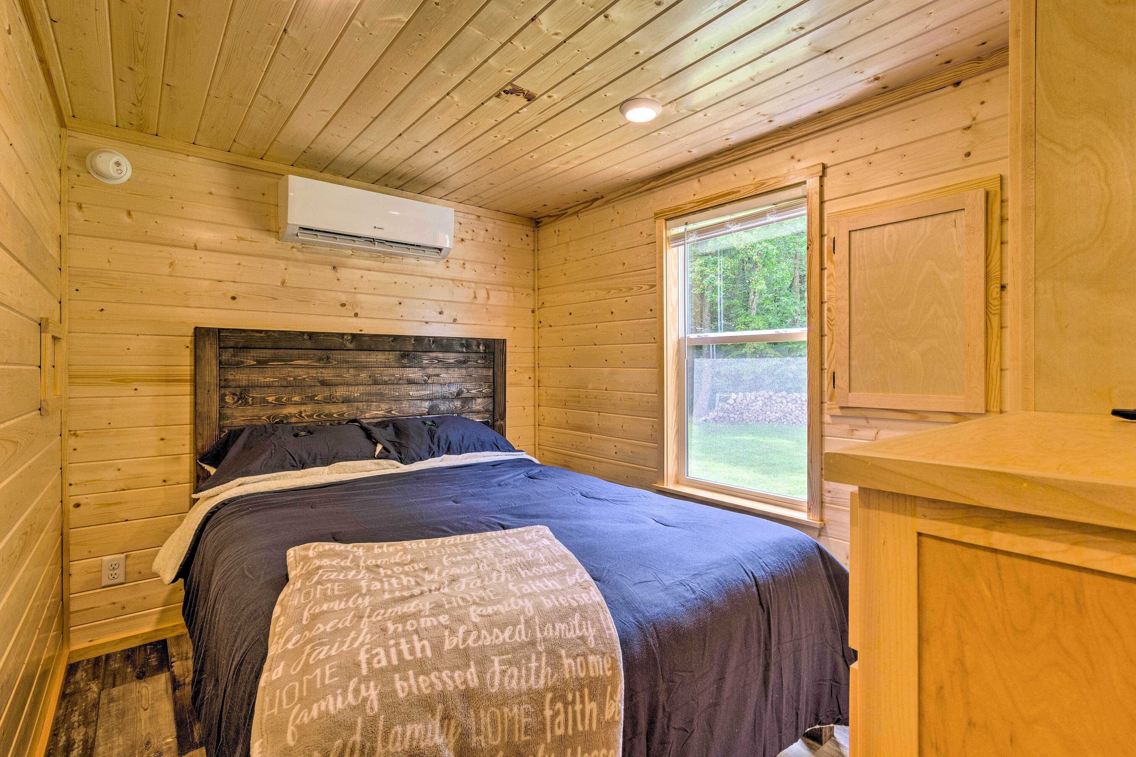 A wooden cabin bedroom with a bed, a window, and an air conditioning unit.