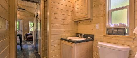 Une salle de bain rustique, aménagée dans une cabane en bois, avec un lavabo, des toilettes et une fenêtre.