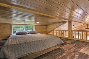 A wooden cabin bedroom with a bed, a window, and a balcony.