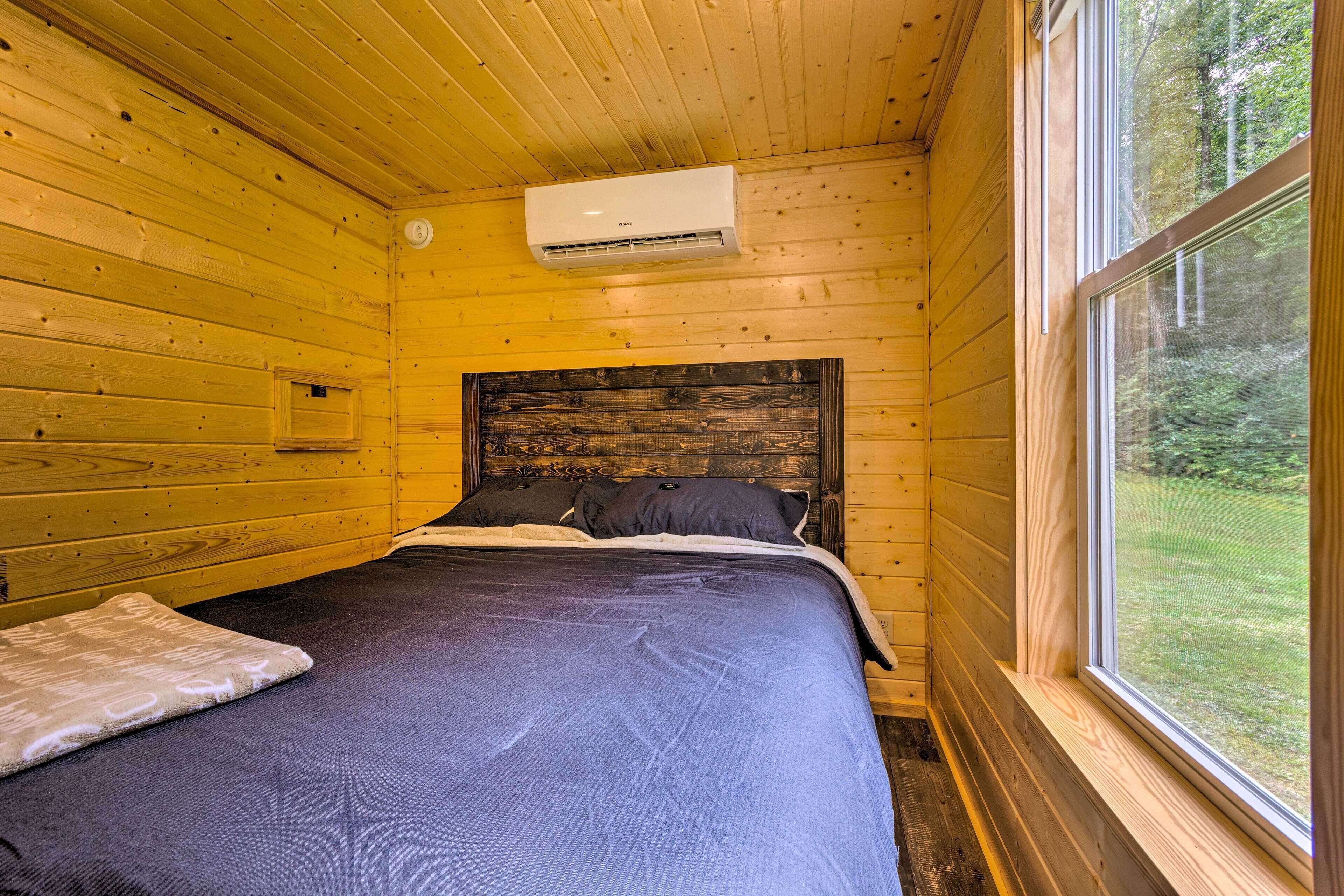 A wooden cabin room with a bed, a window, and an air conditioning unit.