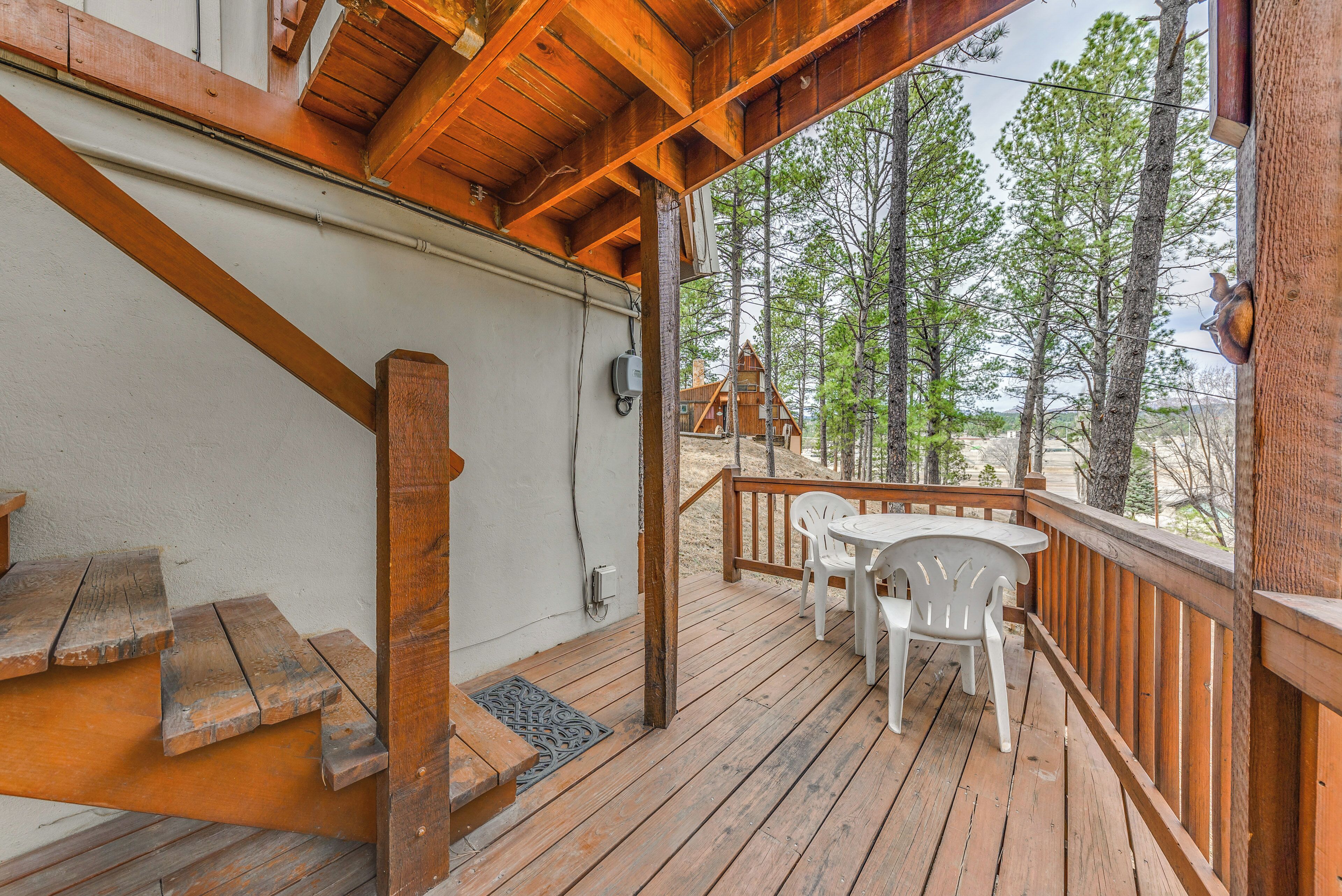 Une terrasse en bois avec une table et des chaises, un escalier et une vue sur les arbres.