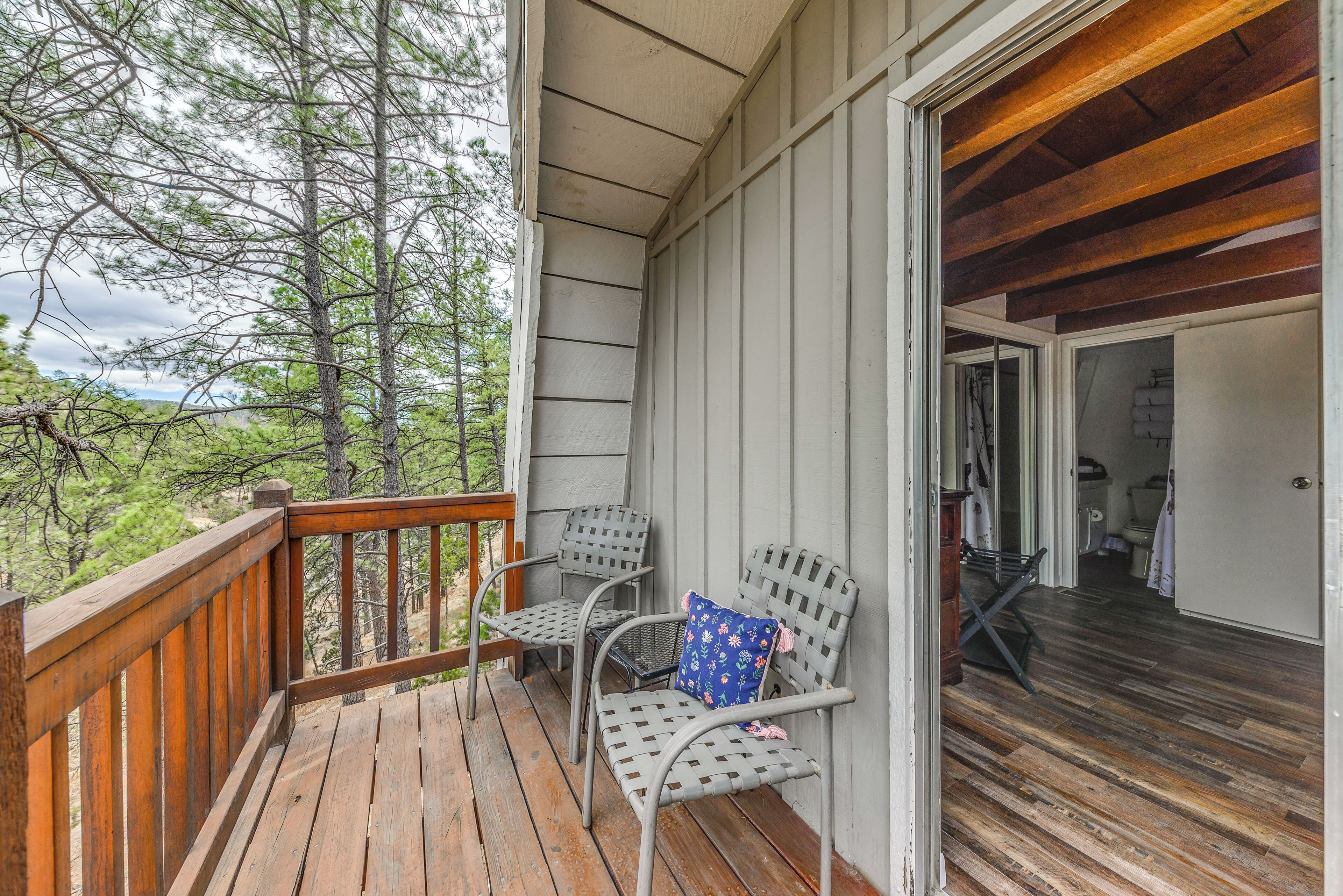 A wooden deck with two metal chairs and a bench, overlooking a forested area.