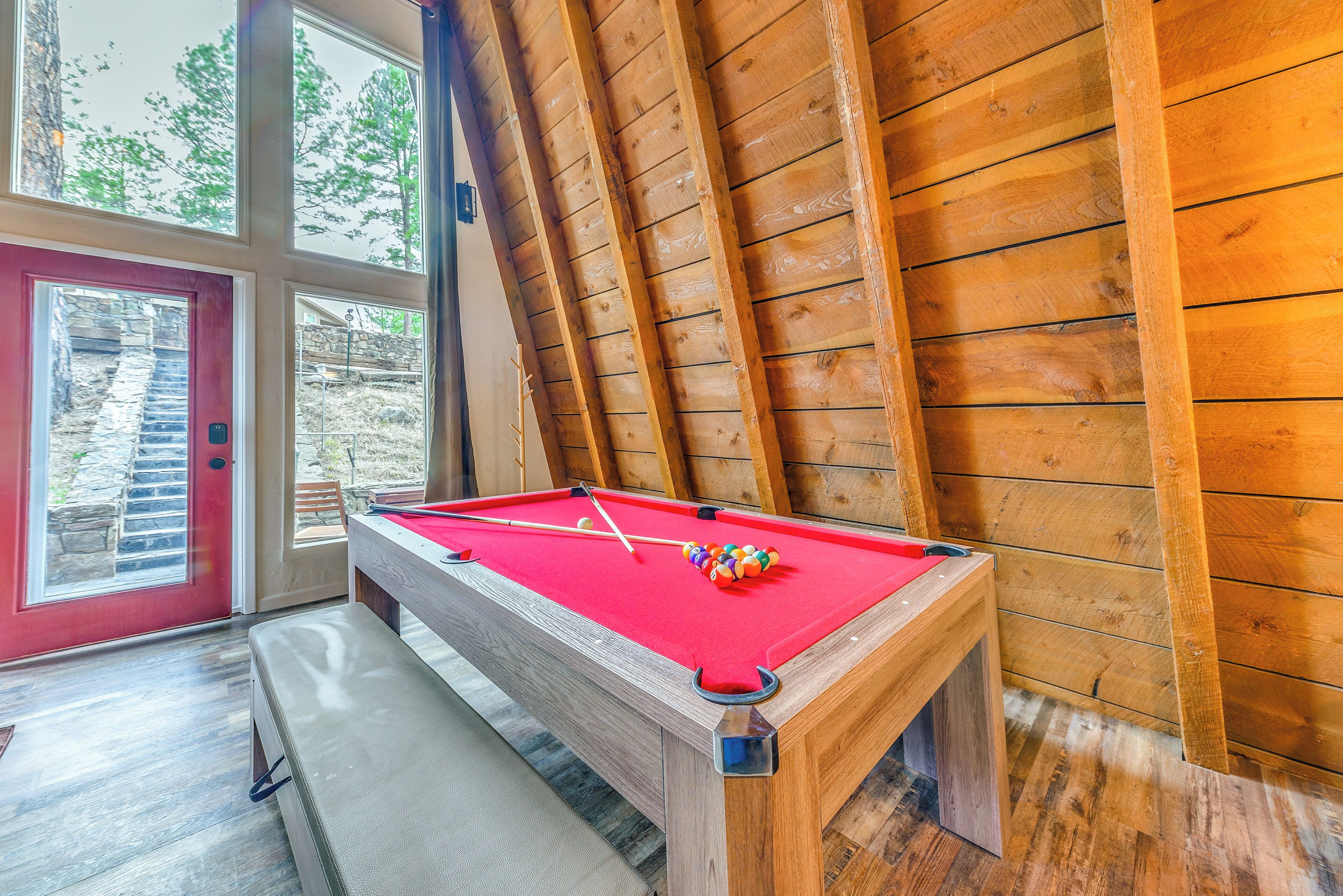 Une table de billard dans une pièce aux murs en bois et aux grandes fenêtres.