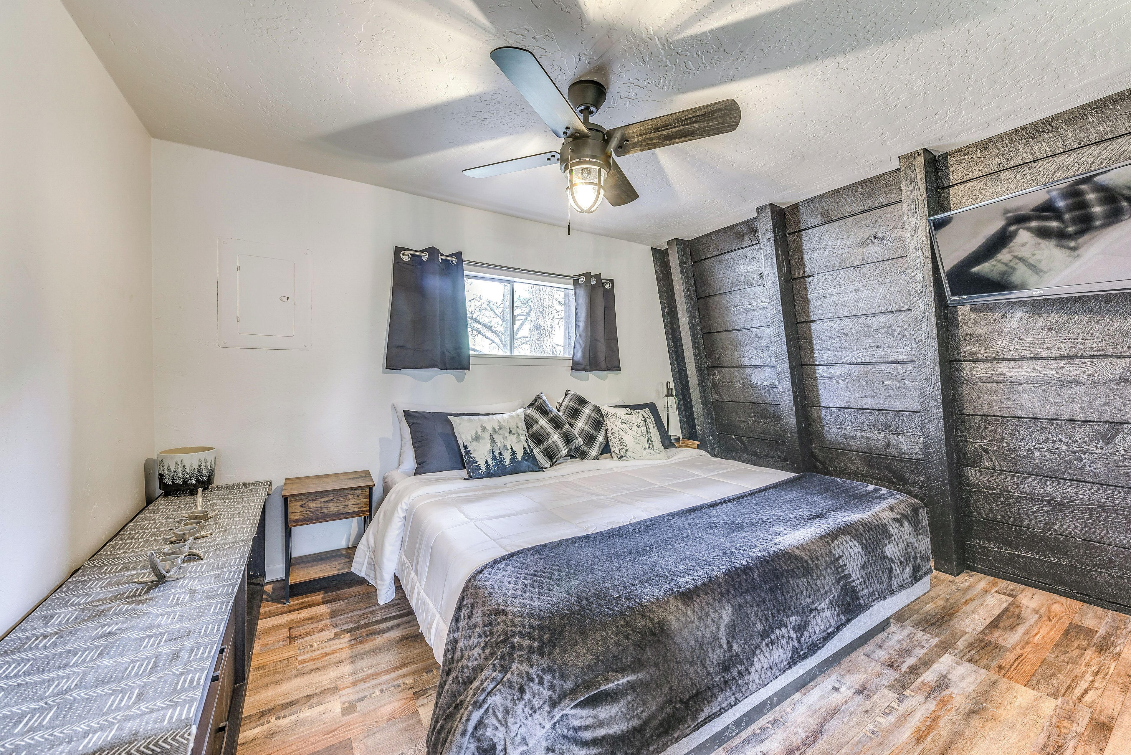 A bedroom with a bed, a desk, a ceiling fan, a window, and wooden walls.