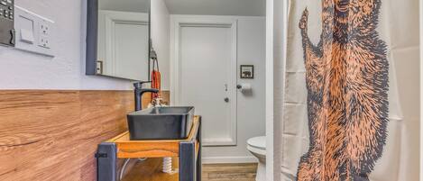 Un baño con tocador de madera, lavamanos negro, espejo y cortina de ducha con diseño de perro.