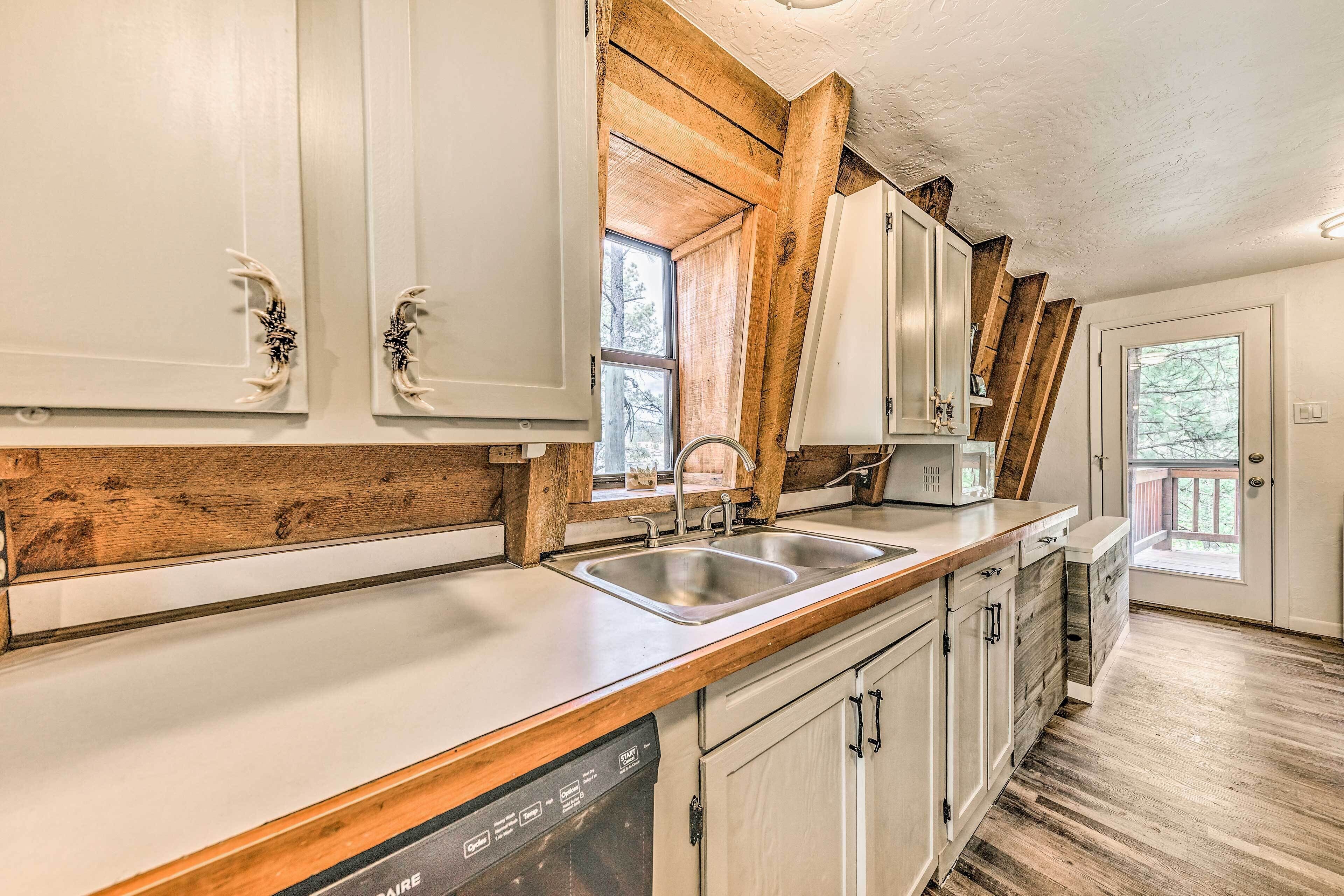 A kitchen with white cabinets, wooden beams, a stainless steel sink, and a dishwasher.