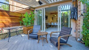 A covered patio with wooden flooring, a table, two chairs, and a potted plant.