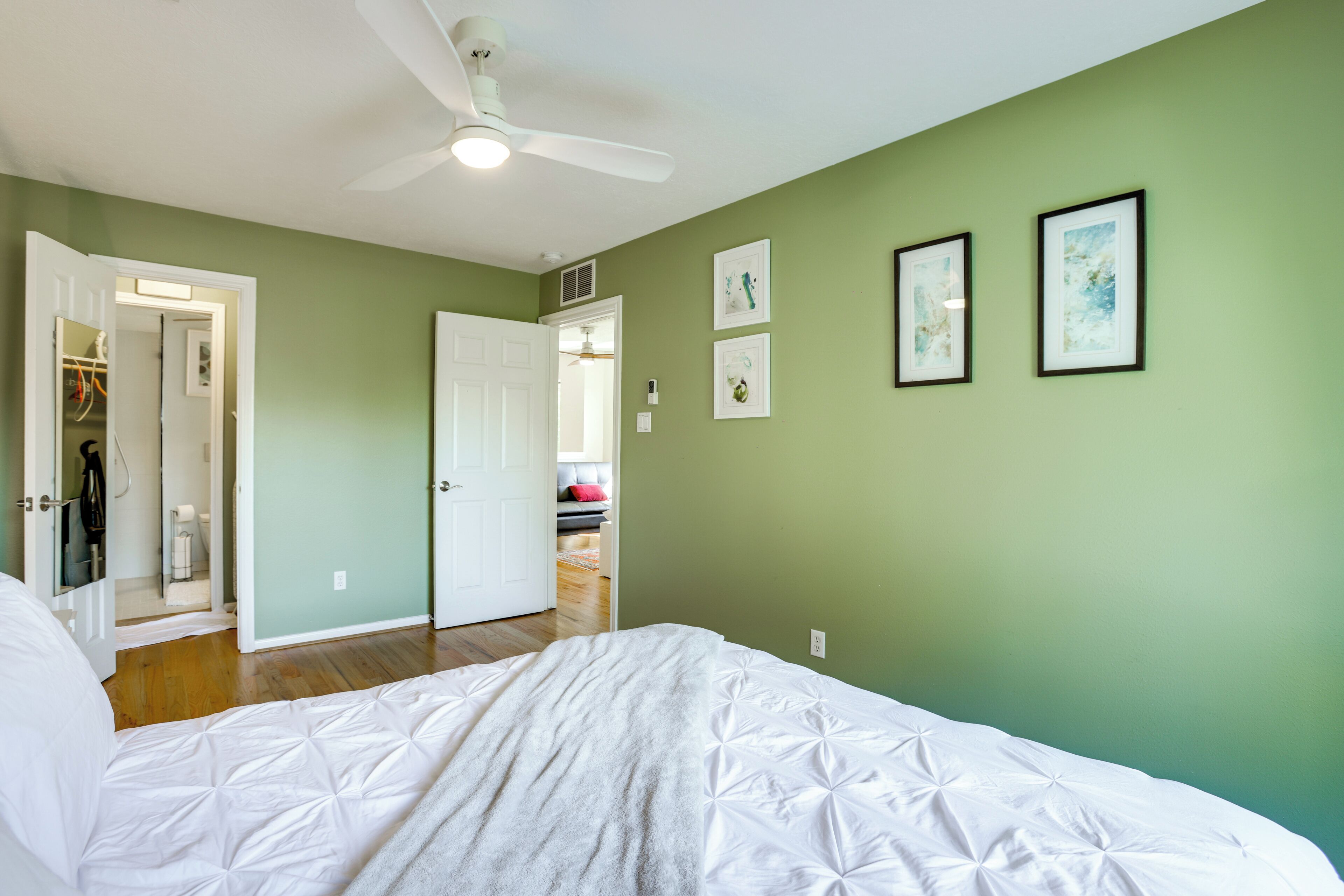 Ein Schlafzimmer mit einem Bett, einem Deckenventilator und einer grünen Wand mit gerahmten Bildern.