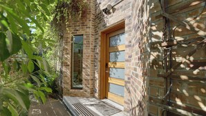 A brick building with a wooden door and window, surrounded by greenery.