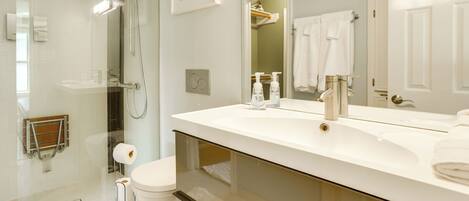 A modern bathroom with a glass-enclosed shower, a white sink, and a large mirror.